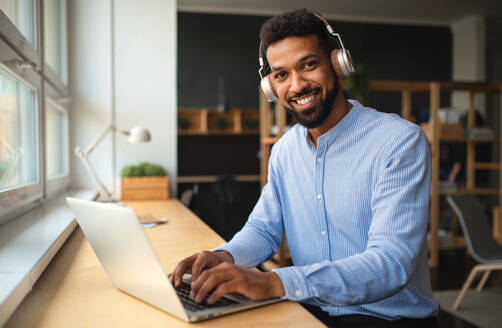 A young African-american teacher with headset and laptop indoors in staffroom looking at camera. - HPIF07898