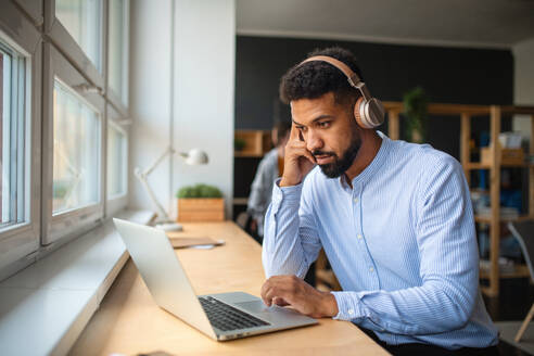 A young African-american teacher with headset and laptop indoors in staffroom. - HPIF07899