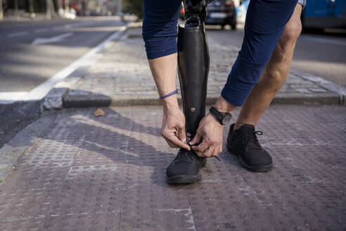 Mann mit amputiertem Bein bindet Schnürsenkel auf Gehweg - JJF00340