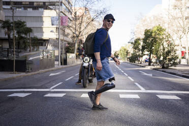 Lächelnder reifer Mann mit amputiertem Bein beim Überqueren der Straße in der Stadt - JJF00342