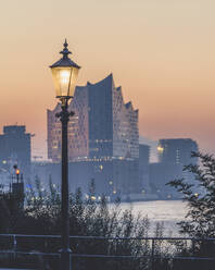 Deutschland, Hamburg, Straßenlaterne leuchtet gegen Elbphilharmonie im Hintergrund in der Abenddämmerung - KEBF02616