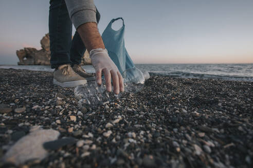 Hand eines Mannes, der eine Plastikflasche am Strand aufhebt - DMGF01042