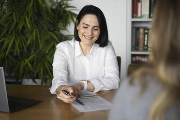 Lächelnde Geschäftsfrau im Gespräch mit einem Kunden am Schreibtisch - NJAF00260