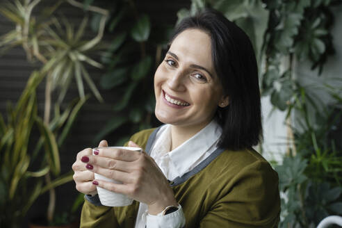 Glückliche Frau mit Kaffeetasse vor Pflanzen - NJAF00265