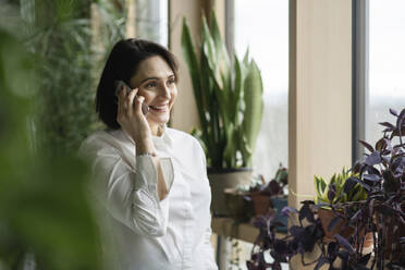 Lächelnde Frau, die bei Pflanzen mit einem Smartphone spricht - NJAF00270