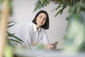 Kontemplative Frau mit Smartphone vor einer Wand - NJAF00272