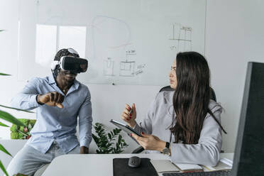 Architekt hält Tablet-PC und diskutiert mit einem Kollegen, der ein Virtual-Reality-Headset trägt, im Büro - OSF01403