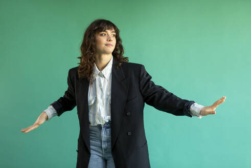 Young woman wearing blazer gesturing against green background - AXHF00295