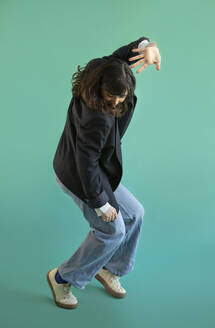 Woman wearing blazer dancing against green background - AXHF00297