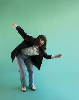 Young woman wearing blazer dancing against green background - AXHF00298
