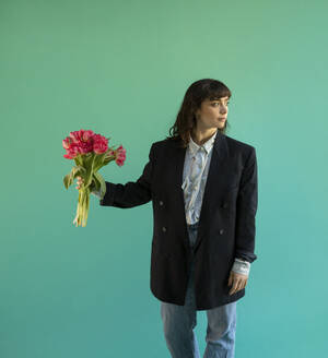 Woman wearing blazer holding bunch of pink tulips against green background - AXHF00300