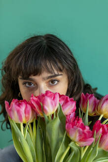 Woman covering face with tulips against green background - AXHF00302