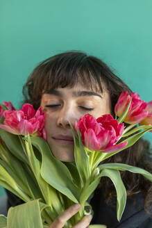 Woman with eyes closed holding tulips against green background - AXHF00303