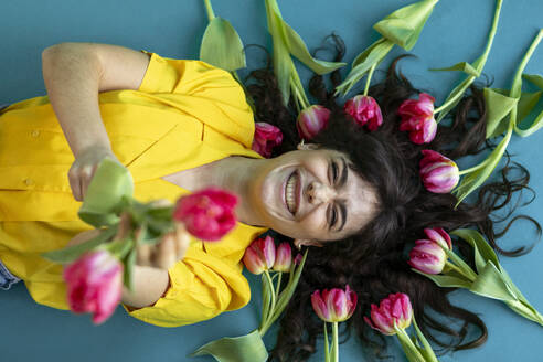 Cheerful woman amidst pink tulips lying on green background - AXHF00305