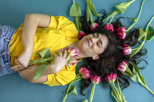 Frau mit geschlossenen Augen liegend inmitten von Tulpen auf grünem Hintergrund - AXHF00306