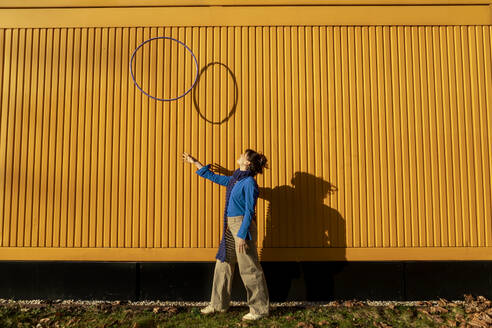 Young woman tossing hula hoop near yellow container on sunny day - AXHF00314