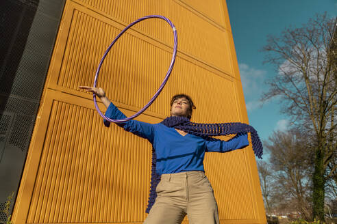 Woman playing with hula hoop near yellow container - AXHF00315