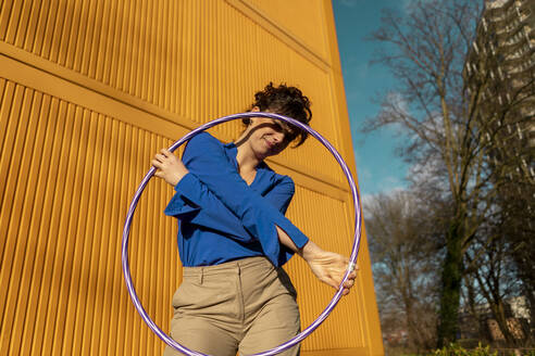 Young woman holding plastic hoop near yellow container - AXHF00316