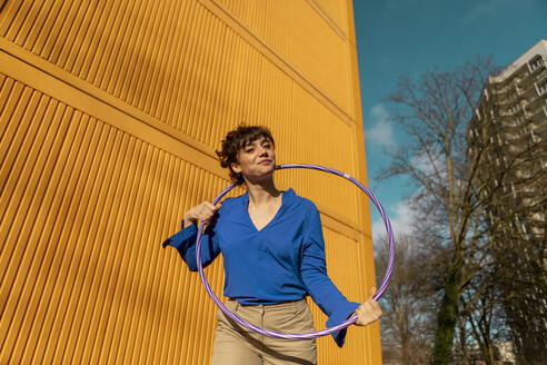 Woman with hula hoop near yellow cargo container on sunny day - AXHF00318