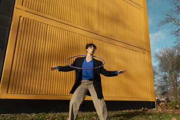 Woman playing with hula hoop in front of yellow container - AXHF00323