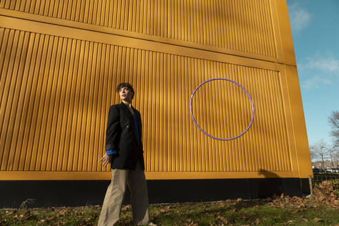 Woman standing by hula hoop in front of yellow cargo container - AXHF00325