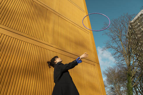 Woman throwing plastic hoop in front of yellow cargo container - AXHF00326