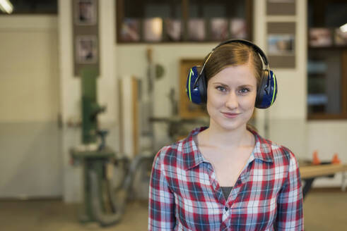 Smiling craftswoman wearing ear protectors in workshop - PAF01976