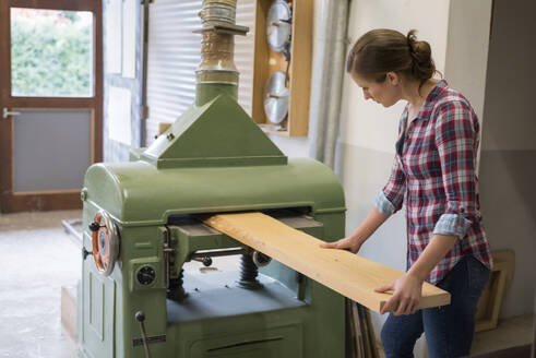 Craftswoman cutting plank through machine in woodshop - PAF01985