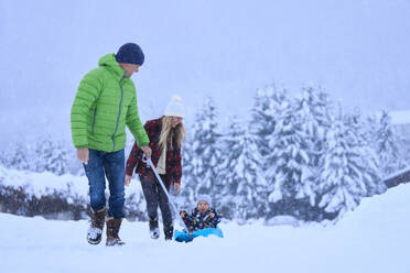 Mutter und Vater mit Sohn auf dem Schlitten sitzend im Schnee - JAHF00185