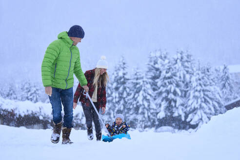 Mother and father with son sitting on sled in snow - JAHF00185