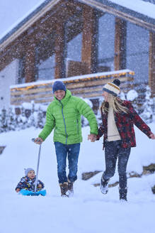 Glücklicher Vater und Mutter mit Sohn auf dem Schlitten sitzend im Schnee - JAHF00186