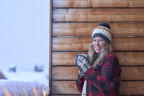 Smiling mature woman wearing knit hat standing in balcony - JAHF00191