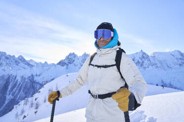 Smiling mature man wearing ski goggles standing in snow - JAHF00203