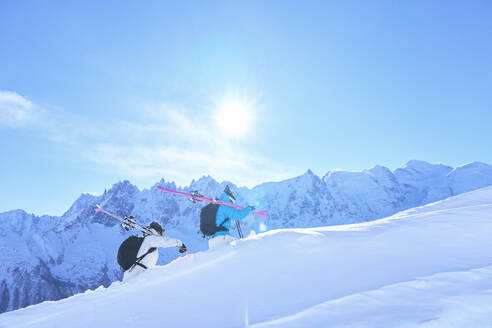 Mature woman and man carrying skies and walking on snowcapped mountain - JAHF00216