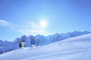 Frau und Mann tragen Skier und gehen auf einem schneebedeckten Berg - JAHF00217