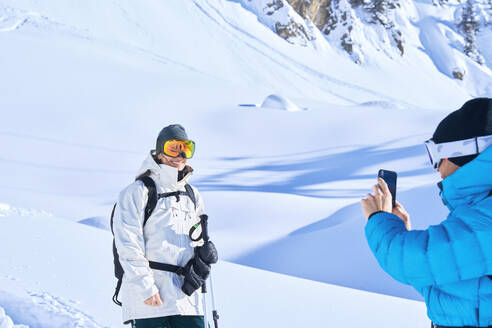 Mature man photographing woman through smart phone in snow - JAHF00235