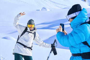 Mature man photographing happy woman through smart phone in snow - JAHF00236