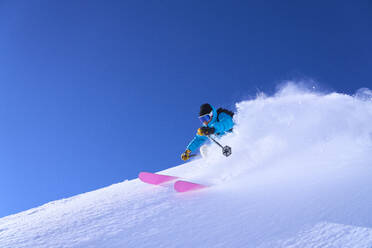 Mann beim Skifahren bergab auf Schnee unter blauem Himmel - JAHF00248