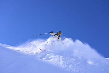 Ältere Frau beim Skifahren bergab unter blauem Himmel - JAHF00252