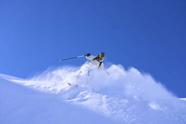 Mature woman skiing downhill under blue sky - JAHF00252