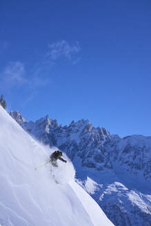 Mann beim Skifahren bergab unter blauem Himmel - JAHF00255