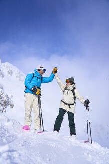 Paar in Skikleidung gibt sich auf einem schneebedeckten Berg die Hand - JAHF00269