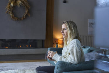 Nachdenkliche Frau mit Kaffeetasse auf dem Sofa zu Hause - JAHF00289