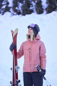 Smiling woman with skis standing in snow - JAHF00306