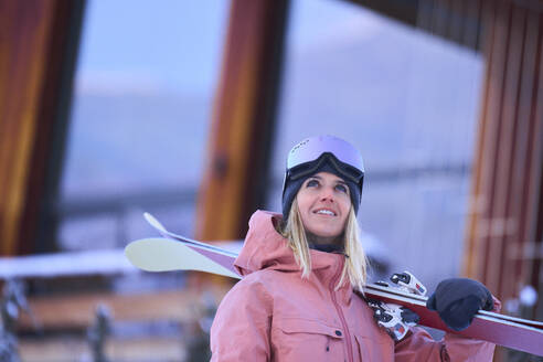 Glückliche Frau mit Skiern vor einem Chalet - JAHF00309