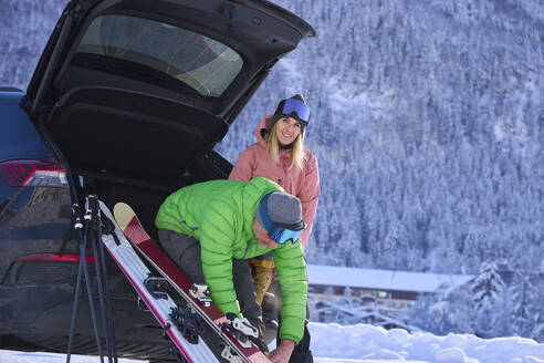 Lächelnde Frau und Mann mit Skiern, die im Kofferraum eines Autos sitzen - JAHF00314