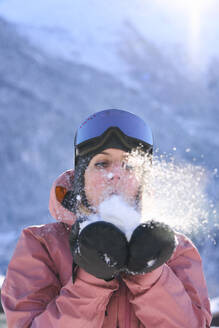 Woman wearing gloves blowing on snow - JAHF00316