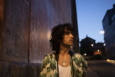 Contemplative young man standing by wall at dusk - AXHF00348