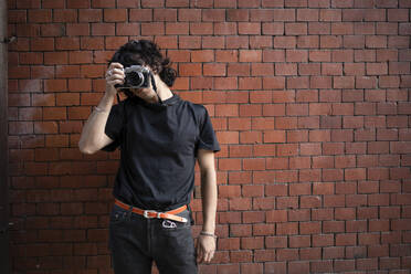 Man photographing through camera in front of brick wall - AXHF00354