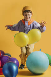 Glücklicher Junge spielt mit bunten Luftballons vor gelbem Hintergrund - VSNF00580